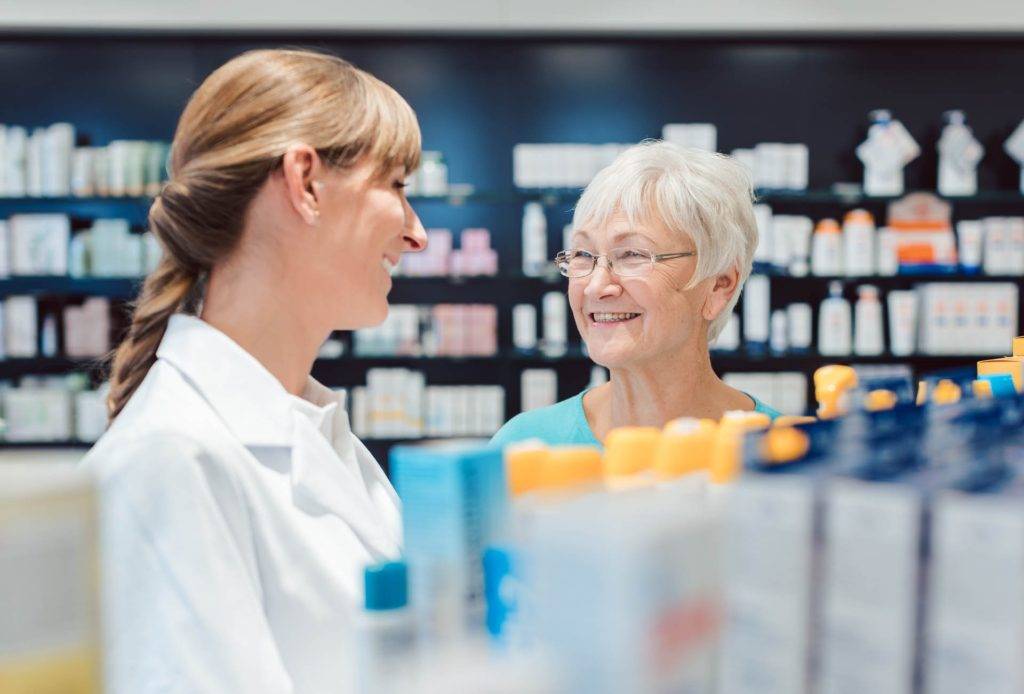 Chemist and customer standing in pharmacy between the shelves