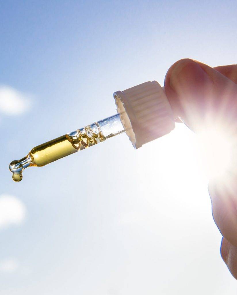 Hand holding dropper pipette with nice golden liquid D-vitamin against sun and blue sky on sunny day. Vitamin D keeps you healthy while lack of sun in winter, cure concept.