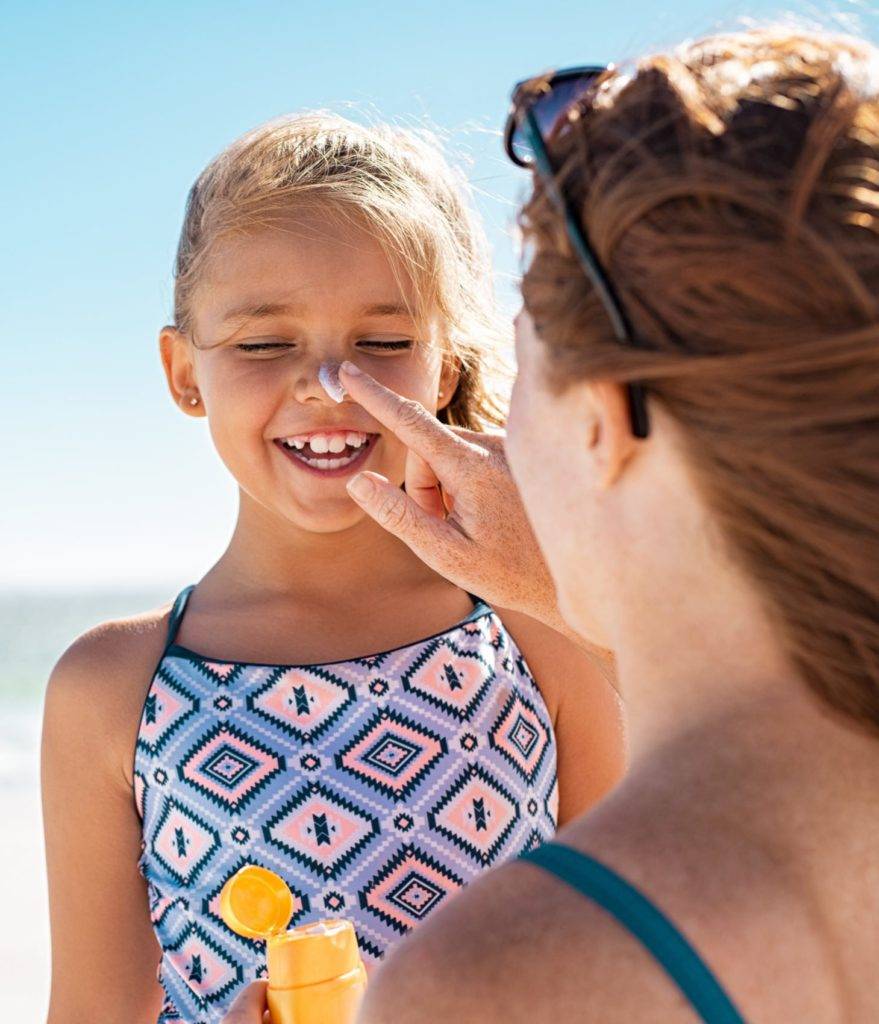 Mother applying suntan lotion on daughter face
