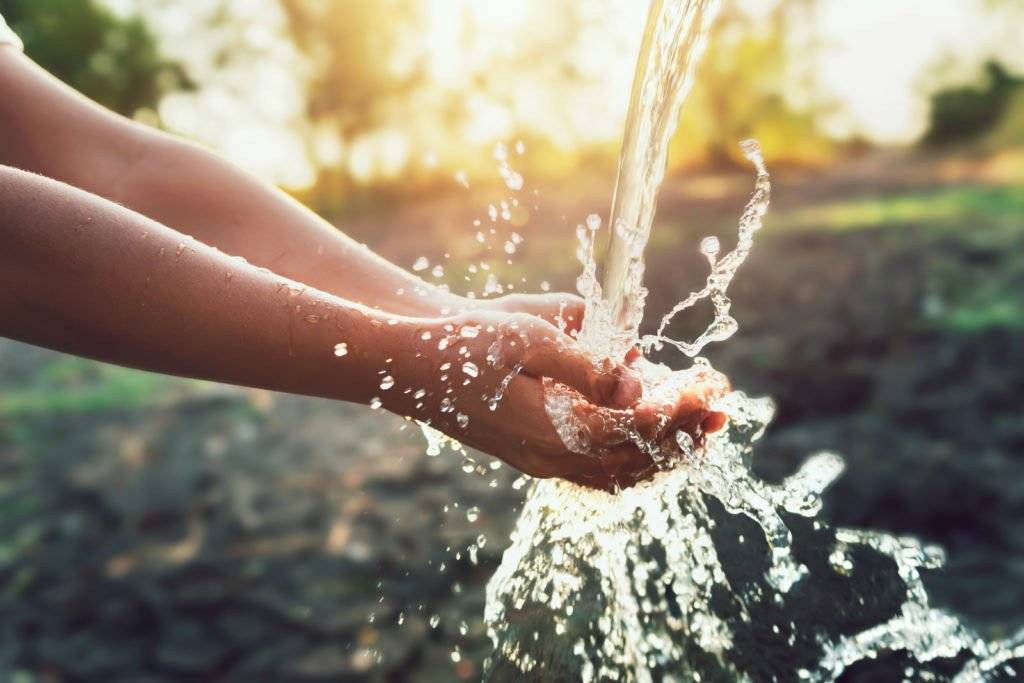 Wasser spritzt in die Hände im Garten