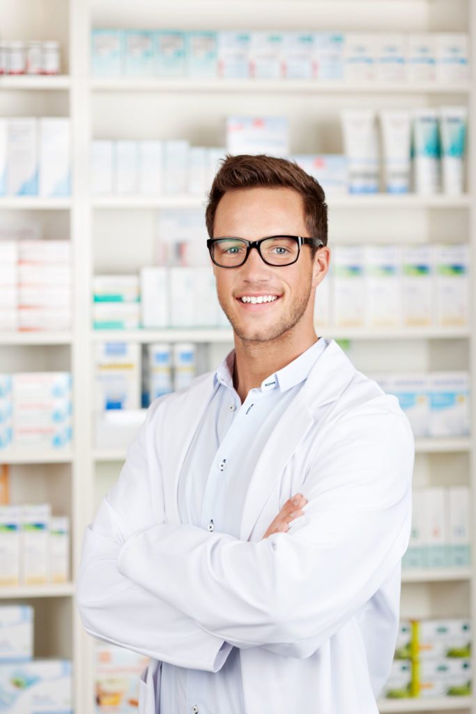 Apotheker*In mit weißem Kittel steht vor Medikamentenregal - Freie Vollzeitstelle als pharmazeutisch kaufmännische Assistenz. Karriere in der Borromäus Apotheke in Salzburg.